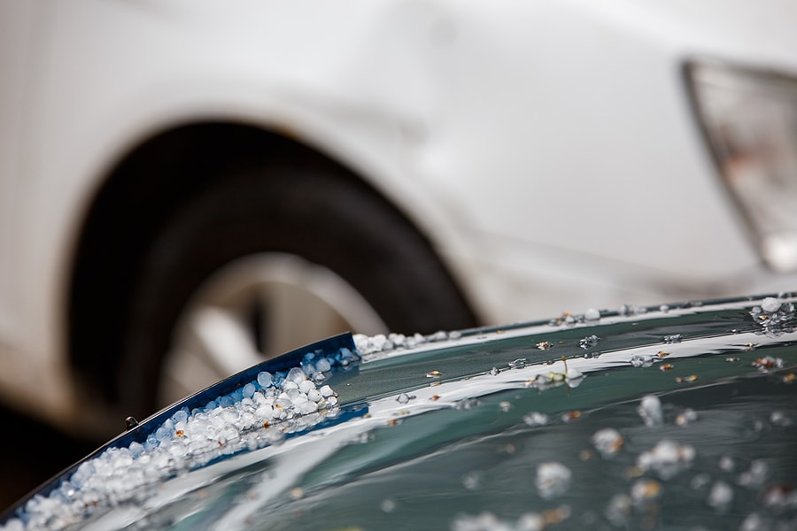 Close-up image of small hail ice balls on green car hood after heavy summer with selective focus at daylight.